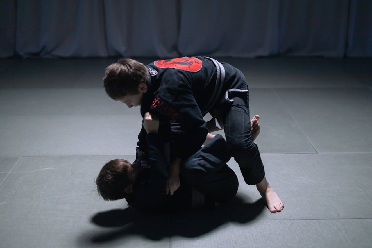 Two boys engaged in jiu jitsu sparring indoors, showcasing martial arts skills.