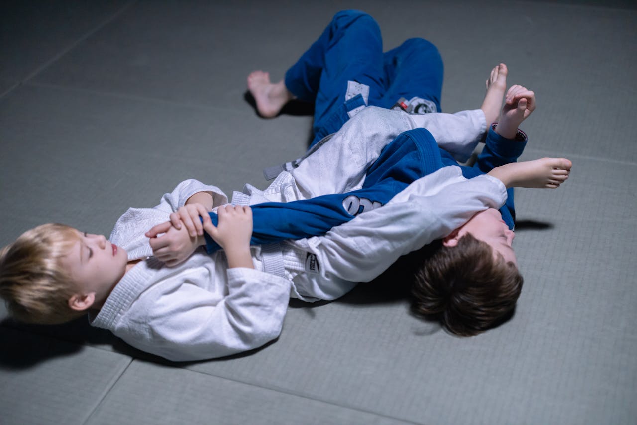 Two young boys practicing judo grappling techniques indoors on a mat.